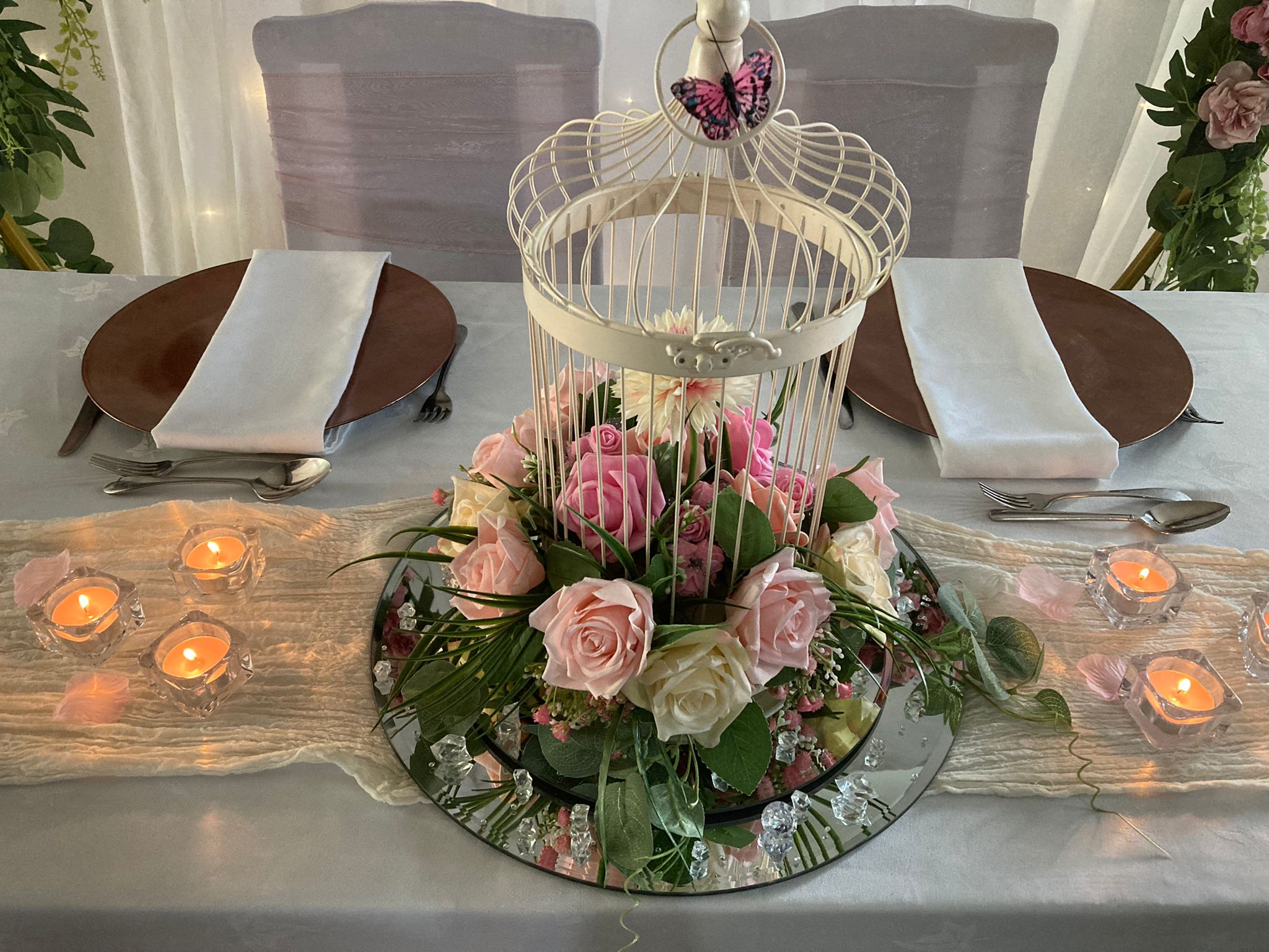 Bird cage centrepiece with pink floral garland on a mirror plate