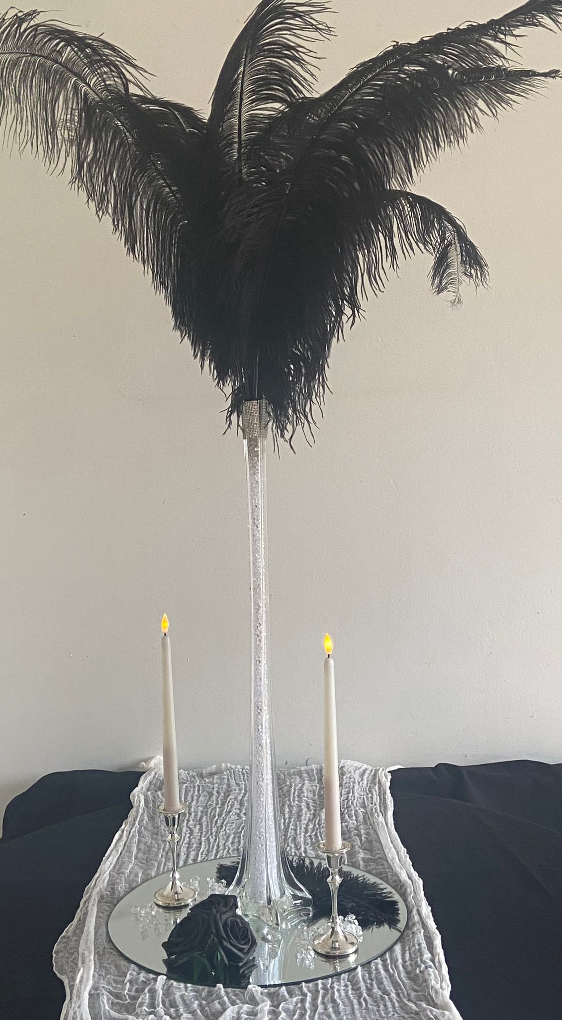 Tall thin glass vase with lots of black feathers