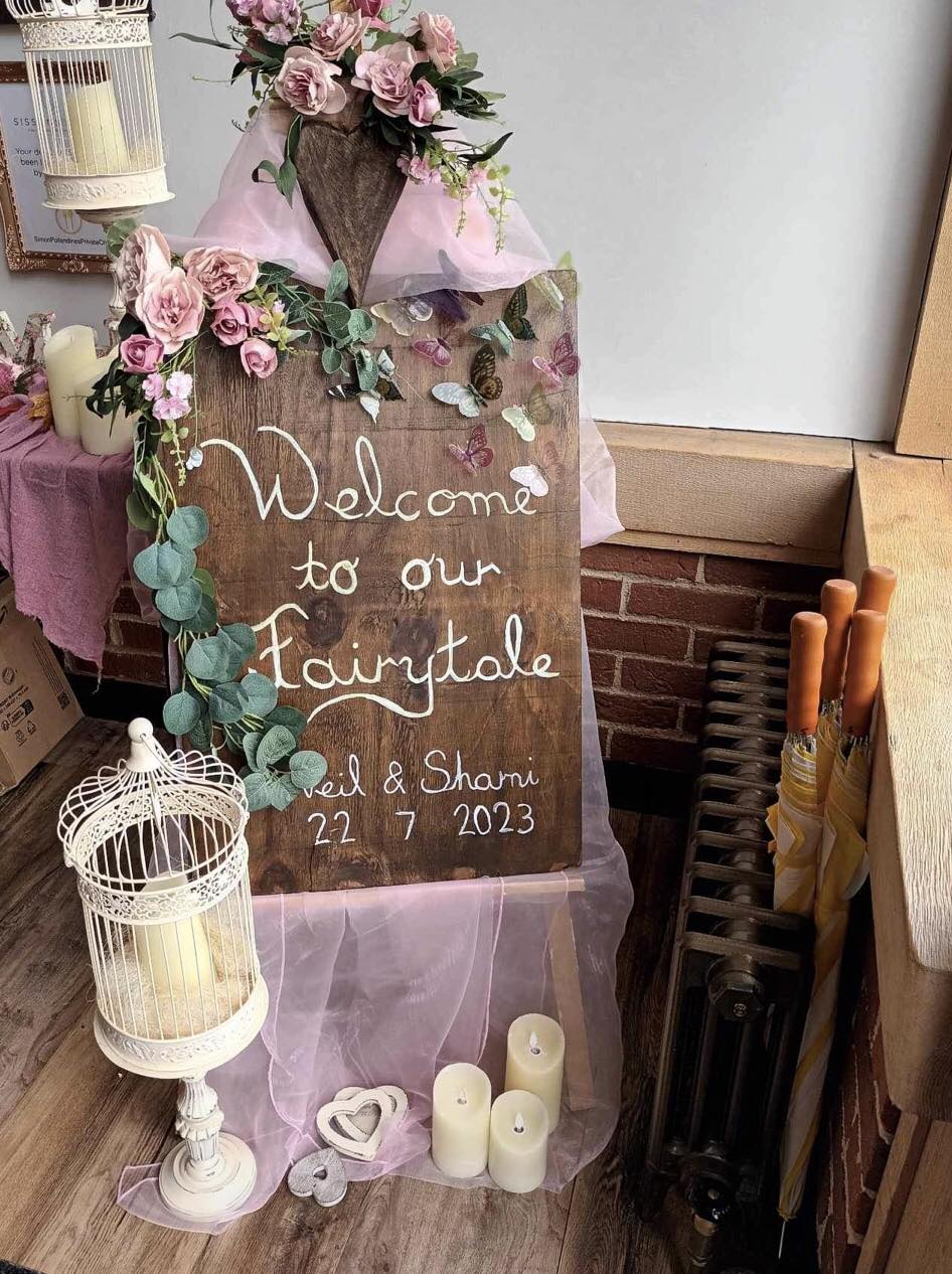 Wooden board, welcome to our fairytale, with pink swag and roses, surrounded by candles
