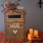 Rustic wooden post box with 3 pillar candles and flower display, on a rust orange swag