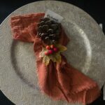 Place setting for Harvest Moon, charger plate with rust orange napkin and fir cone name place setting