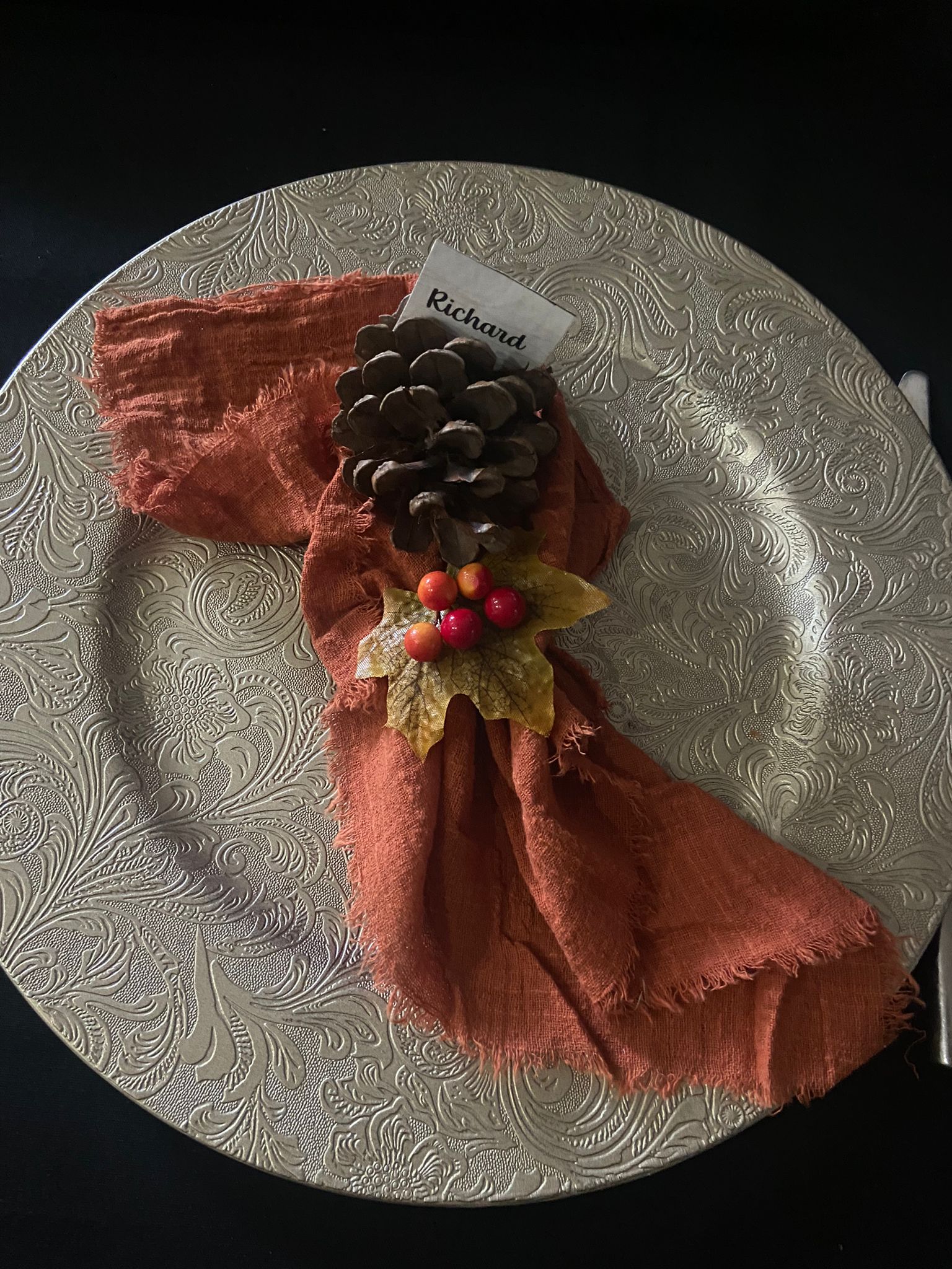 Place setting for Harvest Moon, charger plate with rust orange napkin and fir cone name place setting