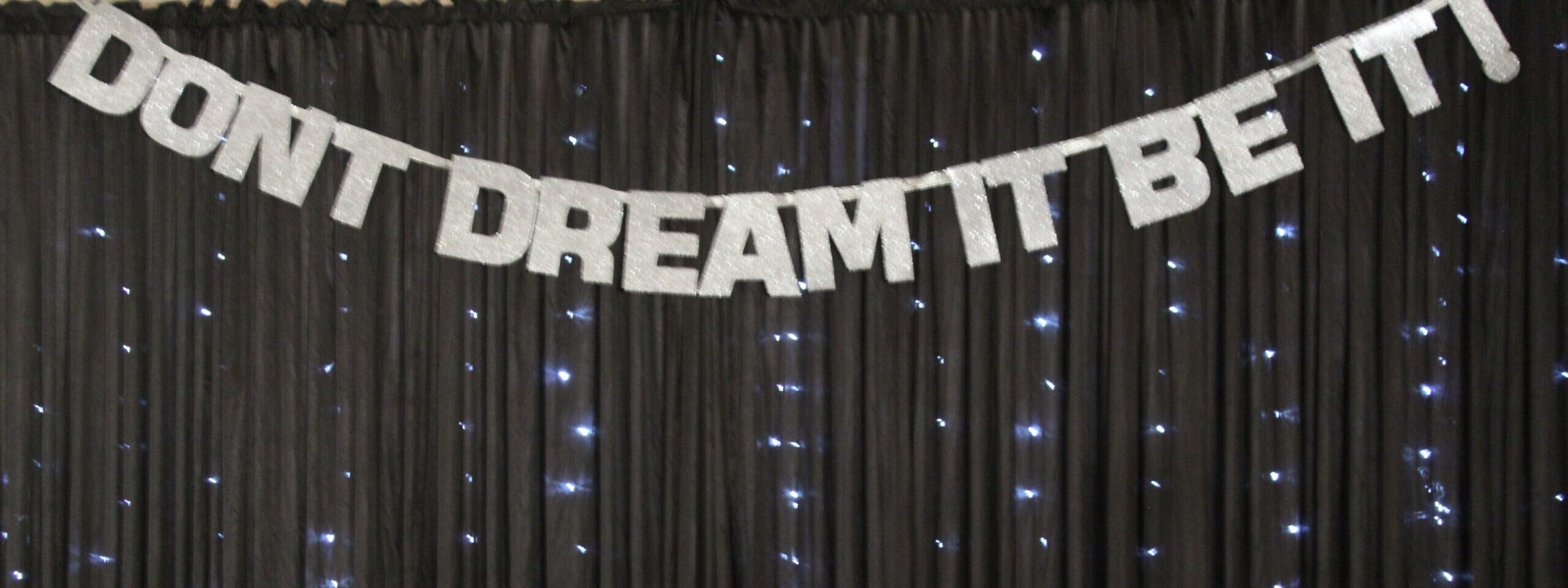 Black starlight sparkle backdrop with don’t dream it be it in silver letters